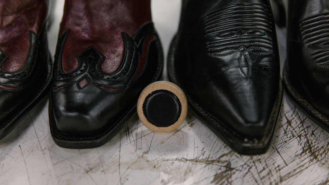 Black cowboy boot and black leather bottle cap.